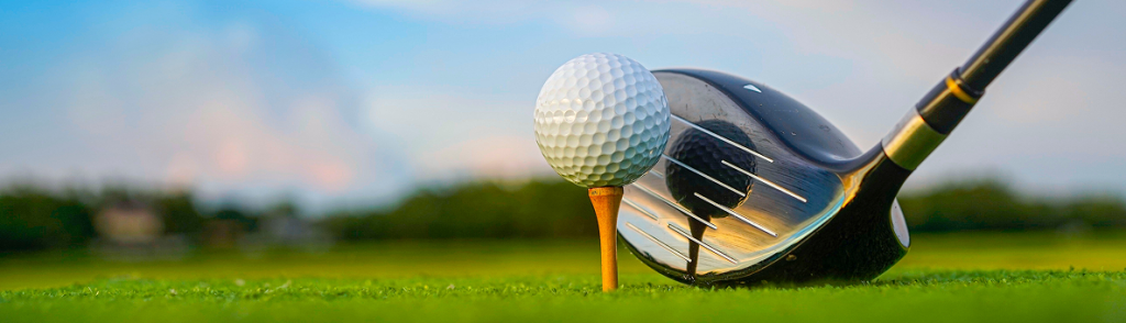 Golf ball on a tee with a driver next to it on a green fairway.